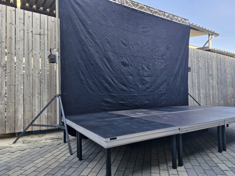 Podium 2x4m inclusief Backdrop Zwarte achterwand op een verhoogd podium, omringd door een houten schutting.