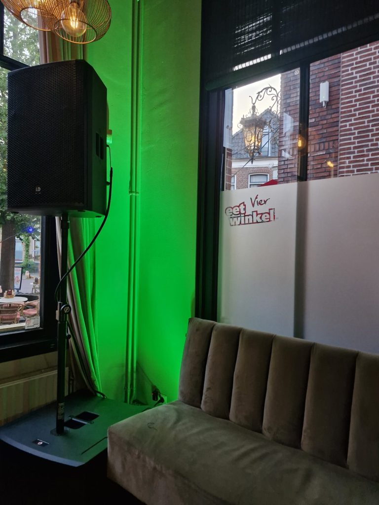 City of Taste | Eetwinkel Vier Hoek van een café met een groene lichtbron en een geluidsinstallatie naast een bank.